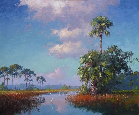 A serene landscape featuring a calm waterway bordered by palm trees and other vegetation under a partly cloudy blue sky.