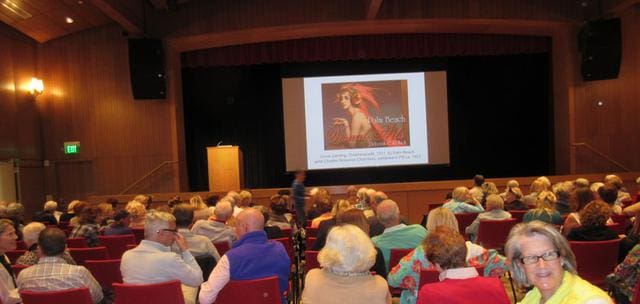 Audience seated in a theater facing a screen displaying a presentation titled "At the Beach: Marilyn Monroe" with an image of Marilyn Monroe on it.